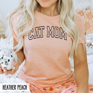 May include: A peach coloured t-shirt with the text "CAT MOM" in black outlined letters.