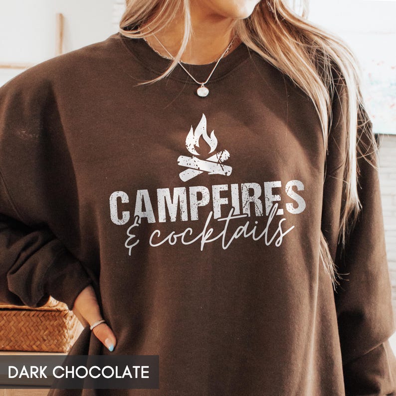 May include: Dark chocolate brown sweatshirt with the text "Campfires & Cocktails" in white, along with a graphic of a campfire. The sweatshirt is a crew neck style.