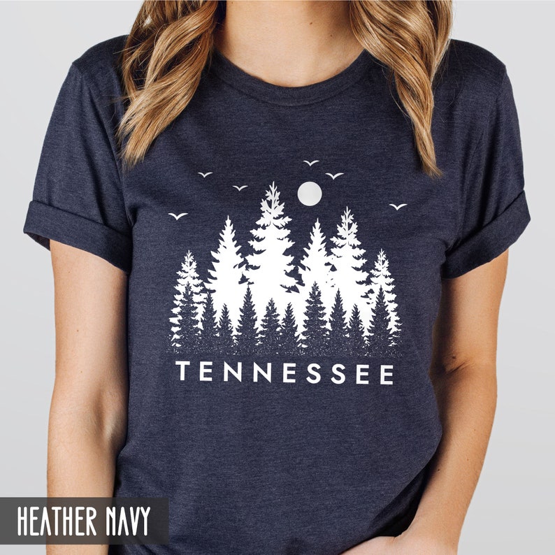 May include: A heather navy blue t-shirt with a white graphic design of a forest silhouette with a moon and birds. The text "TENNESSEE" is printed below the graphic.