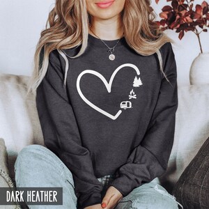 May include: Dark heather grey sweatshirt with a white outline of a heart, a camper, a campfire, and trees inside the heart. The text "DARK HEATHER" is at the bottom of the image.