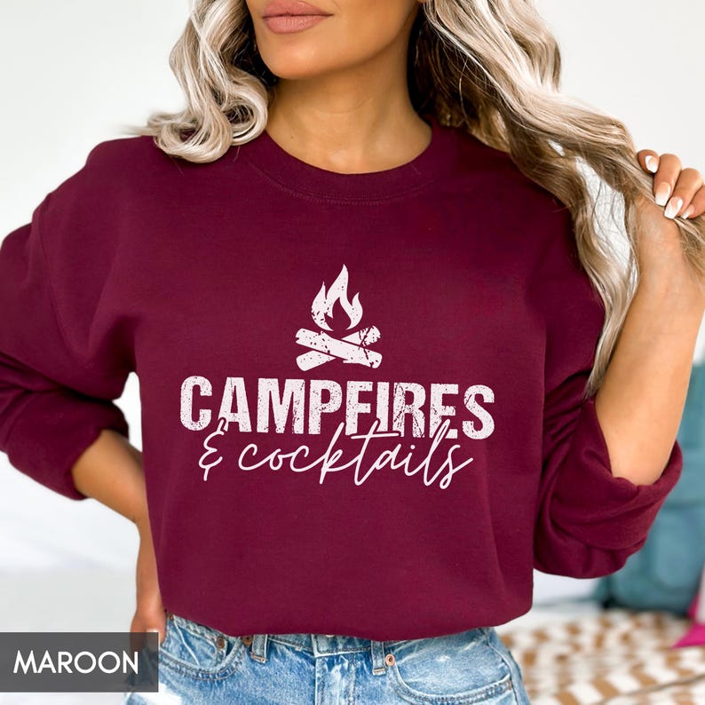 May include: Maroon sweatshirt with the text "Campfires & cocktails" in white. The design includes a campfire graphic above the text. The sweatshirt is a solid maroon color.