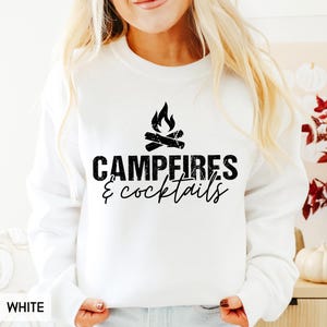 May include: White sweatshirt with the text "Campfires & cocktails" in black, along with a graphic of a campfire. The sweatshirt is a solid white color.