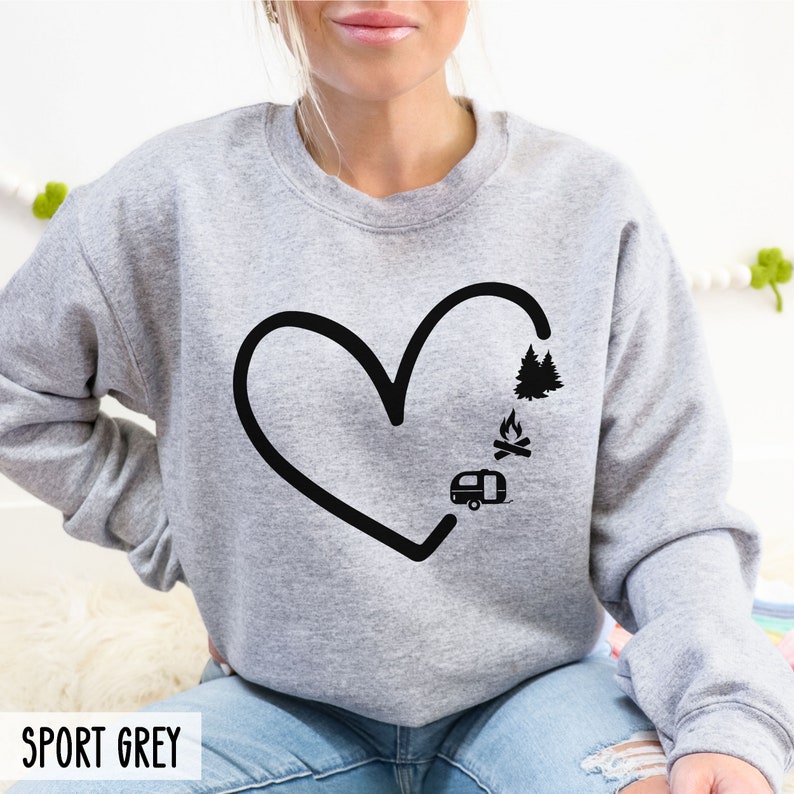 May include: A gray sweatshirt with a black heart design. Inside the heart are images of a camper, a campfire, and pine trees. The text "SPORT GREY" is at the bottom of the image.
