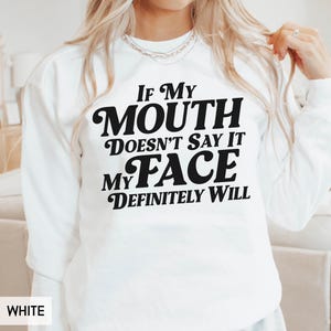 Puede incluir: Sudadera blanca con el texto negro "IF MY MOUTH DOESN'T SAY IT MY FACE DEFINITELY WILL" en negrita y cursiva. La sudadera es de cuello redondo.