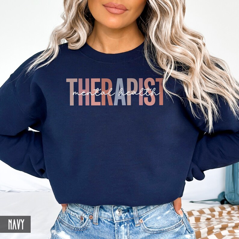 May include: A navy blue sweatshirt with the text "THERAPIST mental health" in a gradient of pink, peach, and gray.