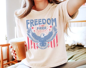 May include: A white t-shirt with a blue and red graphic of an eagle with the words "FREEDOM IS NOT FREE" printed on it.