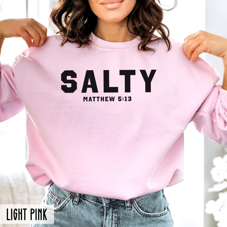 May include: A light pink sweatshirt with the text "SALTY" in black, followed by "MATTHEW 5:13" in smaller black text.
