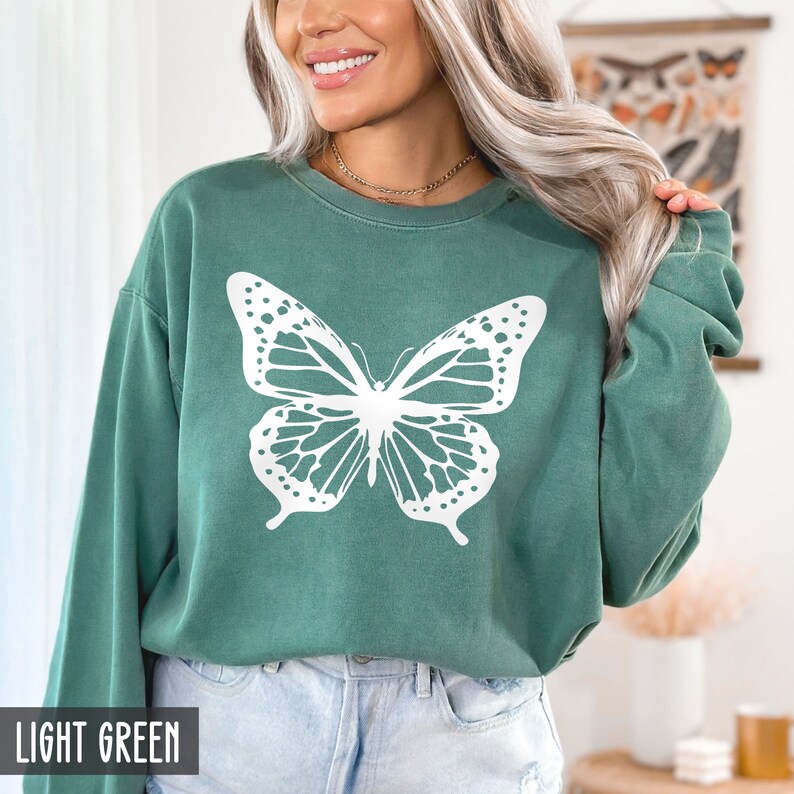 Peut inclure: Un sweat-shirt vert clair avec un motif de papillon blanc. Le sweat-shirt a un col rond et des manches longues.