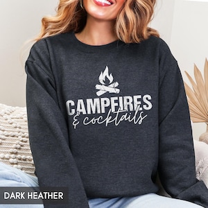 May include: Dark heather gray sweatshirt with the text "Campfires & Cocktails" in white. The design includes a campfire graphic above the text. The sweatshirt is a casual top.