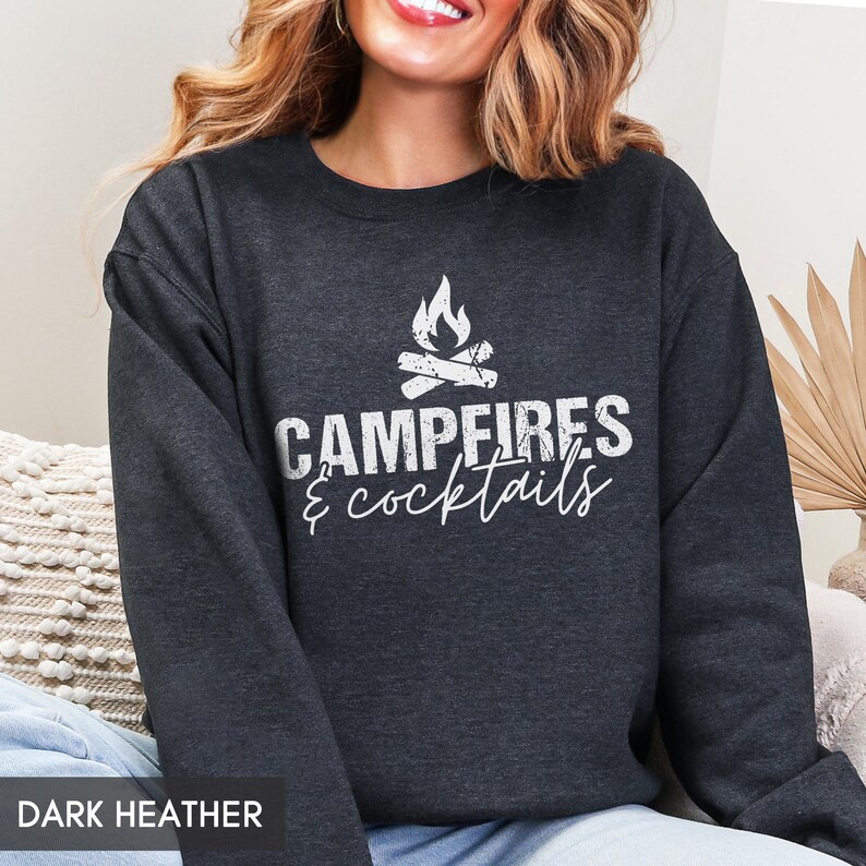 May include: Dark heather gray sweatshirt with the text "Campfires & Cocktails" in white. The design includes a campfire graphic above the text. The sweatshirt is a casual top.