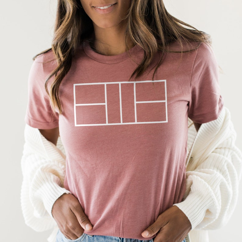 May include: A dusty rose t-shirt with a white tennis court graphic. The shirt has short sleeves and a crew neck.