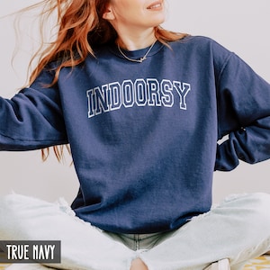 Pode incluir: Uma camisola azul-marinho com a palavra "INDOORSY" impressa em branco na frente. A camisola &eacute; feita de um material macio e confort&aacute;vel e tem um caimento descontra&iacute;do.