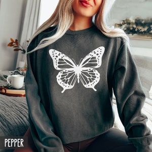 Peut inclure: Un sweat-shirt gris fonc&eacute; avec un motif de papillon blanc. Le sweat-shirt a un col rond et des manches longues.