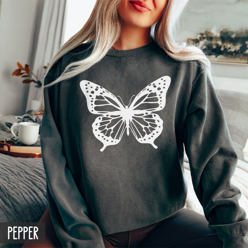 Peut inclure: Un sweat-shirt gris fonc&eacute; avec un motif de papillon blanc. Le sweat-shirt a un col rond et des manches longues.