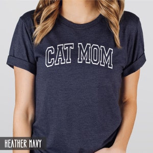 May include: A heather navy blue t-shirt with the text "CAT MOM" in white outlined letters.