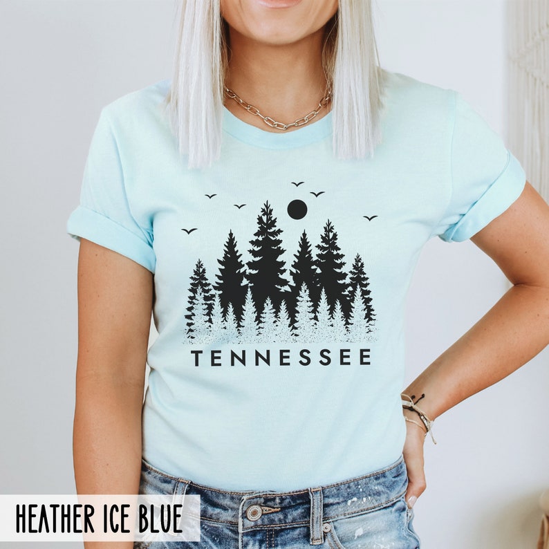 May include: A light blue t-shirt with a black graphic of a forest silhouette and the word "TENNESSEE" printed below. The shirt is made of a soft, comfortable material.