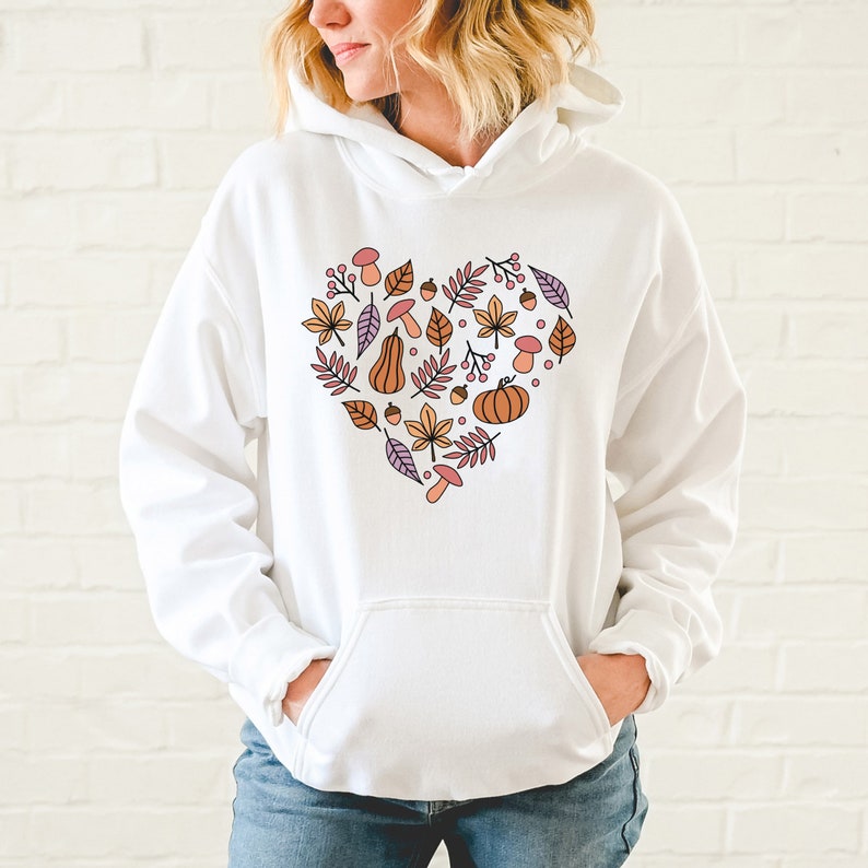 May include: White hoodie with a heart-shaped design featuring autumn-themed elements like leaves, pumpkins, acorns, and mushrooms in shades of orange, pink, and purple.