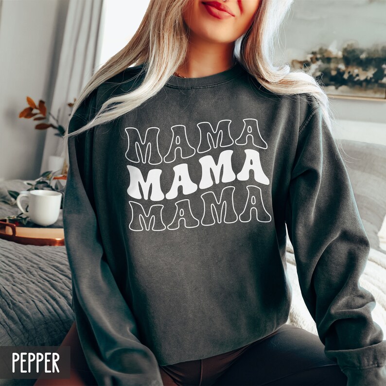 May include: A dark gray sweatshirt with the word "MAMA" repeated three times in a retro font style. The text is white.
