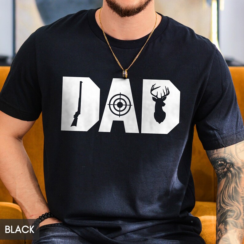 May include: Black t-shirt with the word "DAD" in white block letters. The "D" features a rifle, the "A" a target, and the second "D" a deer silhouette. The word "BLACK" is printed at the bottom left.