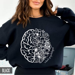May include: Black sweatshirt with a white outline of a brain with flowers on one side and the text "school psychologist" on the other side.