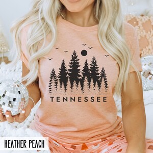 May include: A peach-colored t-shirt with a black silhouette of a forest and a full moon with the word "TENNESSEE" printed below the image.