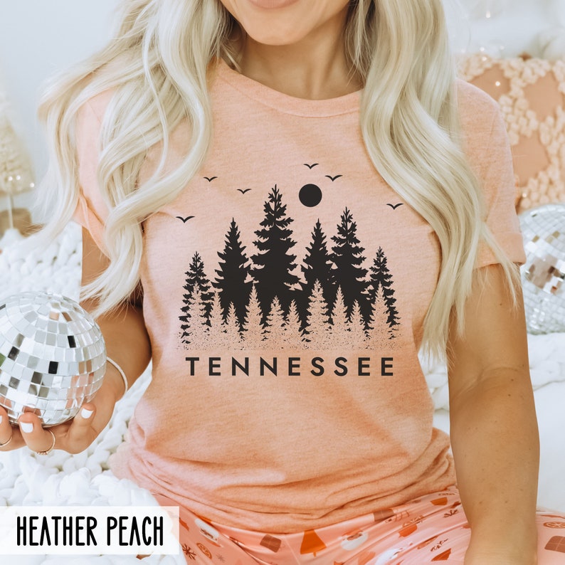 May include: A peach-colored t-shirt with a black silhouette of a forest and a full moon with the word "TENNESSEE" printed below the image.
