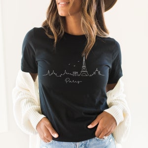 Op de afbeelding: Een zwart T-shirt met een witte omtrek van de Eiffeltoren en het woord "Paris" eronder.