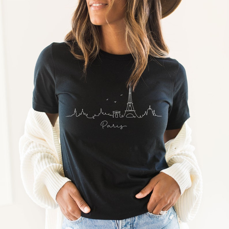Op de afbeelding: Een zwart T-shirt met een witte omtrek van de Eiffeltoren en het woord "Paris" eronder.