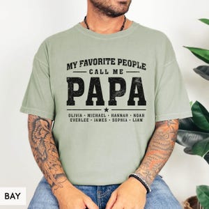A man wearing a green t-shirt with the text "MY FAVORITE PEOPLE CALL ME PAPA" printed on it.