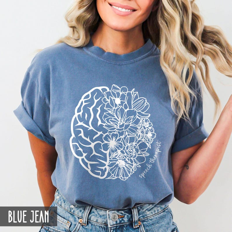 May include: A blue jean t-shirt with a white outline of a brain and flowers. The text "Speech Therapist" is written on the shirt.