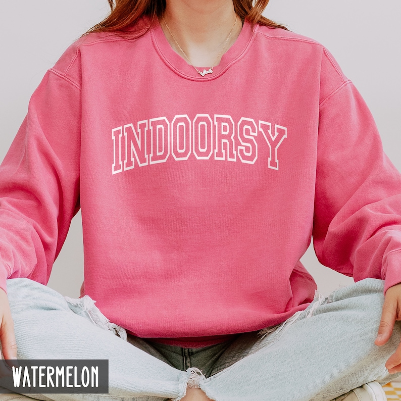 Pode incluir: Uma camisola rosa com o texto "INDOORSY" em letras brancas com contorno. A camisola &eacute; feita de um material macio e confort&aacute;vel e tem um corte descontra&iacute;do.