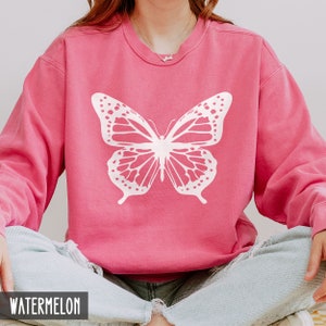 Peut inclure: Un sweat-shirt rose avec un motif de papillon blanc. Le sweat-shirt est fait d'un tissu doux et confortable et a une coupe d&eacute;contract&eacute;e.