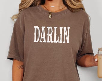 May include: A brown oversized t-shirt with the word "DARLIN" printed in white on the front. The shirt is made of a soft, comfortable material and has a relaxed fit.