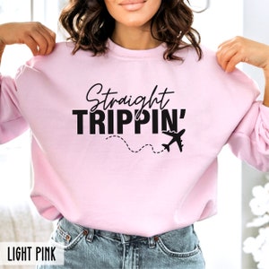 Puede incluir: Sudadera rosa claro con el texto "Straight Trippin'" en letras negras. Un peque&ntilde;o gr&aacute;fico de avi&oacute;n est&aacute; debajo del texto con una l&iacute;nea discontinua que conduce a &eacute;l.