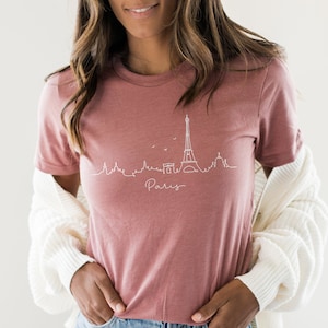 Op de afbeelding: Een mauve t-shirt met een witte omtrek van de Eiffeltoren en het woord "Paris" eronder.