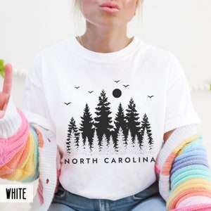 以下が含まれることがあります： 黒い森のシルエットと「NORTH CAROLINA」の文字が書かれた白のTシャツです。