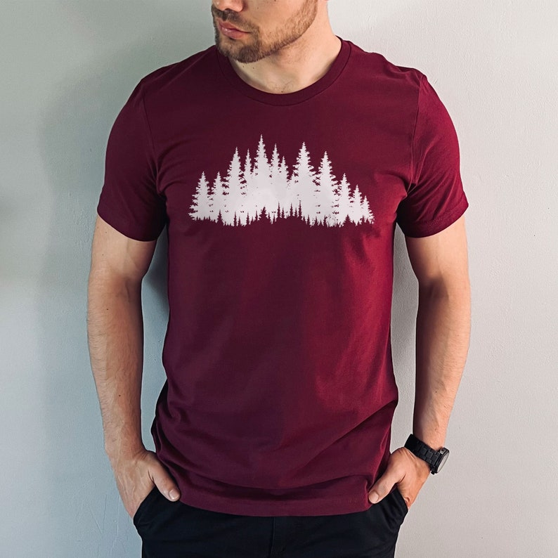 May include: A maroon t-shirt with a white silhouette of a forest on the front.