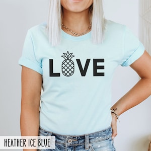 May include: A light blue t-shirt with a black pineapple graphic and the word "LOVE" printed on the front. The shirt is made of a soft, comfortable material.