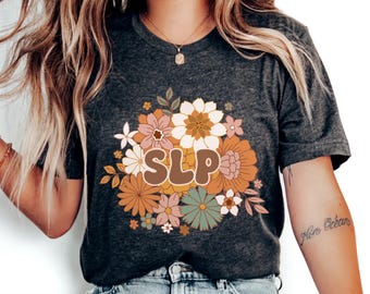 Könnte beinhalten: Ein dunkelgrau meliertes Kurzarm-T-Shirt mit den Buchstaben SLP in einer fetten, abgerundeten Schrift, die mittig von einer Ansammlung illustrierter Blumen in Orange-, Creme-, Rosa- und gedeckten Grüntönen auf der Brust platziert ist.