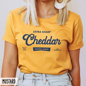 May include: A yellow t-shirt with a blue graphic that says "EXTRA SHARP Cheddar" with the text "NET WT. 8 OZ. (226g) NATURAL CHEESE KEEP REFRIGERATED" underneath.