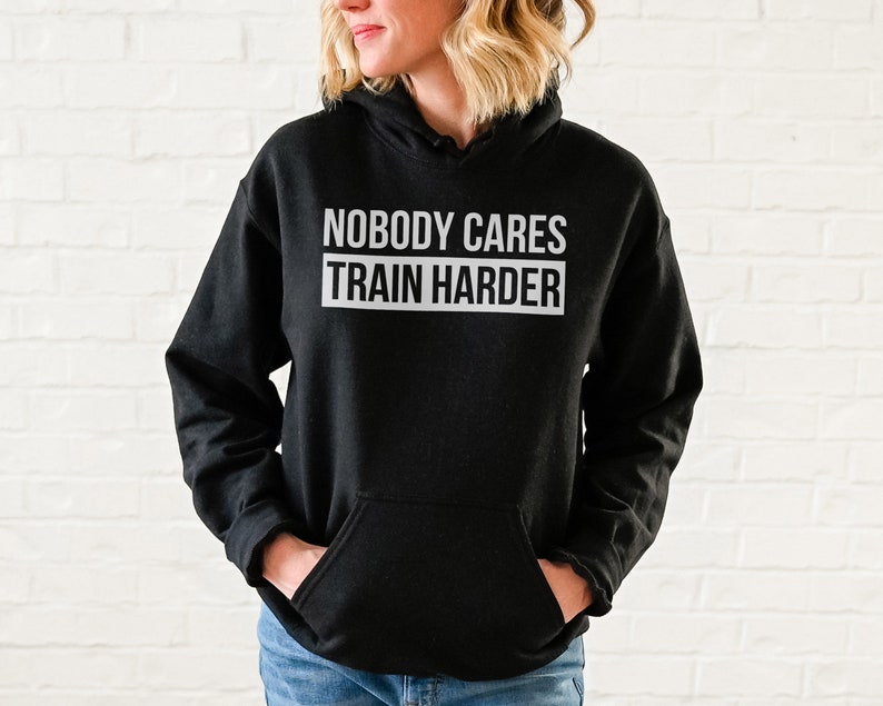 Pu&ograve; includere: Felpa con cappuccio nera con il testo "Nobody Cares Train Harder" in lettere bianche.