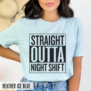 A person wearing a heather ice blue t-shirt with the text STRAIGHT OUTTA NIGHT SHIFT printed in a black boxed design on the front.