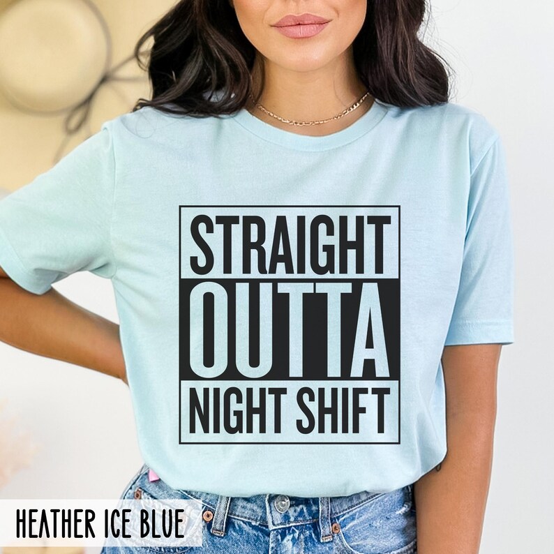 A person wearing a heather ice blue t-shirt with the text STRAIGHT OUTTA NIGHT SHIFT printed in a black boxed design on the front.