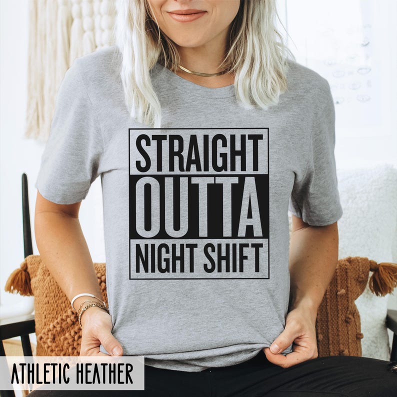 A person wearing an athletic heather grey t-shirt with the text STRAIGHT OUTTA NIGHT SHIFT printed in a black boxed design on the front.