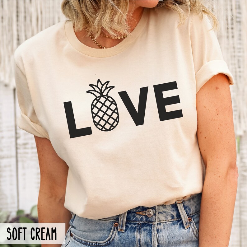 May include: A soft cream colored t-shirt with a black pineapple graphic and the word "LOVE" printed on the front.