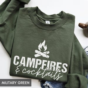 May include: Military green sweatshirt with the words "Campfires & Cocktails" in white script. The design includes a campfire graphic. The sweatshirt is a crew neck style.