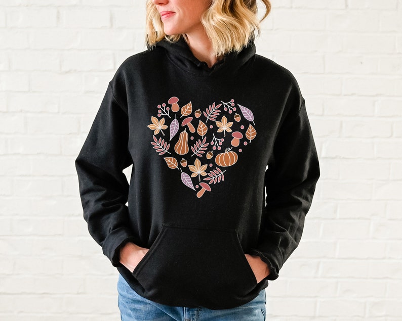 May include: Black hoodie with a heart-shaped design featuring autumn-themed elements like leaves, acorns, mushrooms, and a pumpkin in shades of orange, brown, and pink.