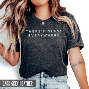 May include: Dark grey heather t-shirt with the text "There's glass everywhere" printed in white.