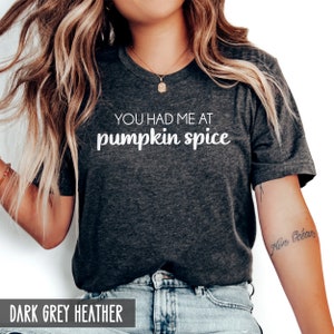 Pode incluir: Uma camiseta cinza escuro heather com o texto "You had me at pumpkin spice" impresso em branco.