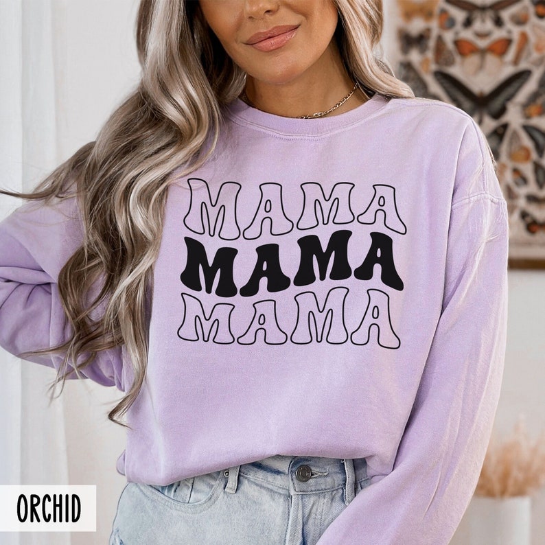 May include: A lavender colored long-sleeved sweatshirt with the text "MAMA" repeated three times in a retro font.